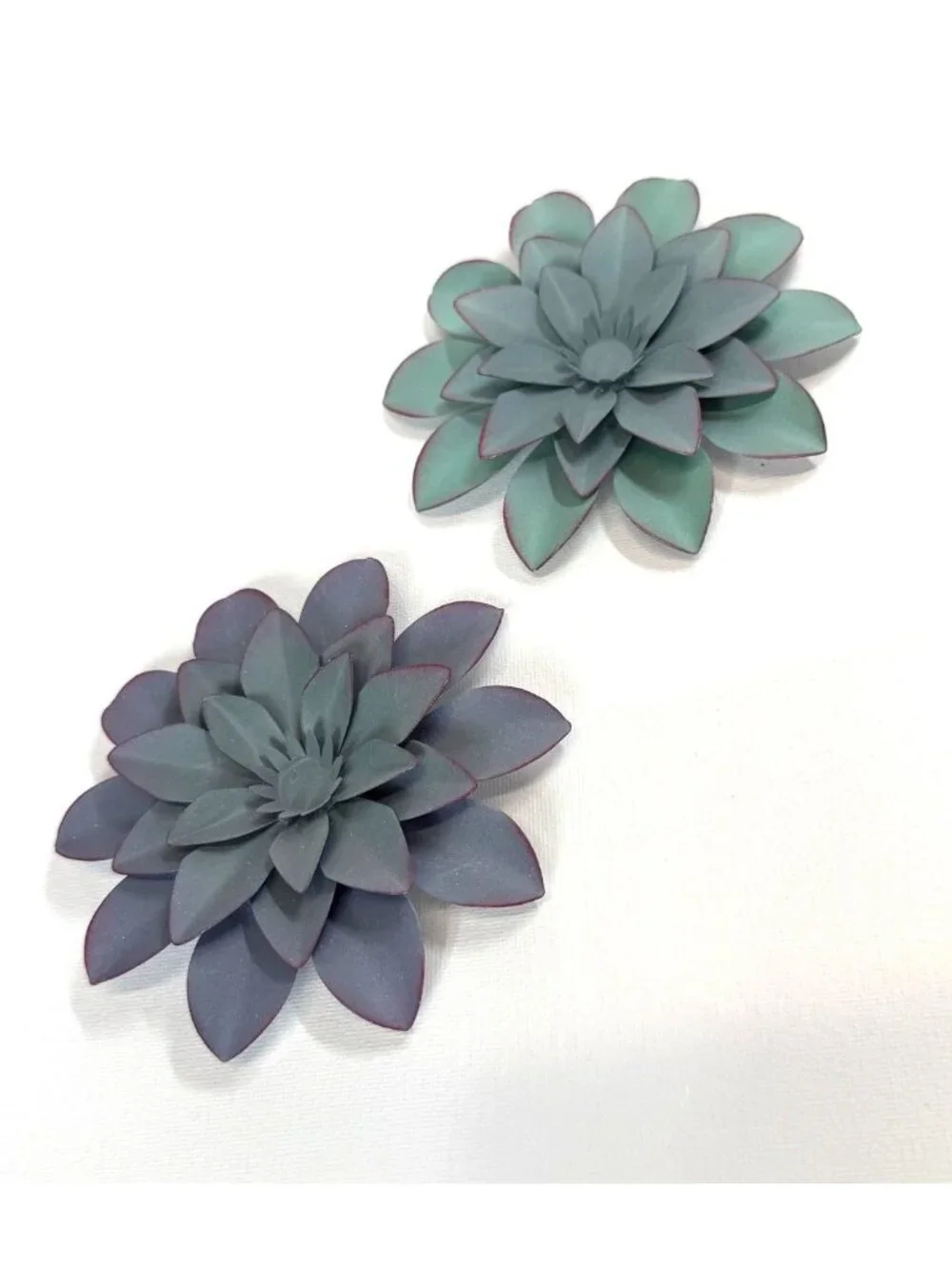 Small, teal-colored metal wall art feature is a layered flower design with disti